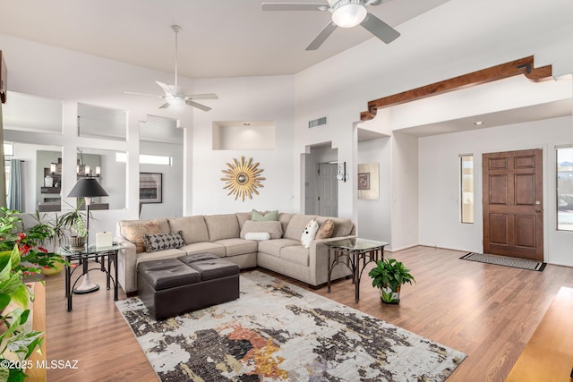 living area with a towering ceiling, a ceiling fan, visible vents, and wood finished floors