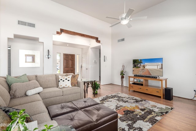 living room featuring light wood-style flooring, a towering ceiling, visible vents, and a ceiling fan