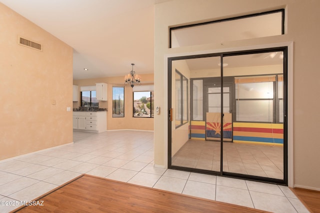 interior space featuring a notable chandelier, light tile patterned floors, visible vents, vaulted ceiling, and baseboards