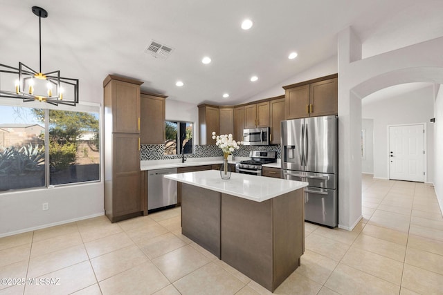 kitchen with vaulted ceiling, a kitchen island, decorative backsplash, hanging light fixtures, and stainless steel appliances