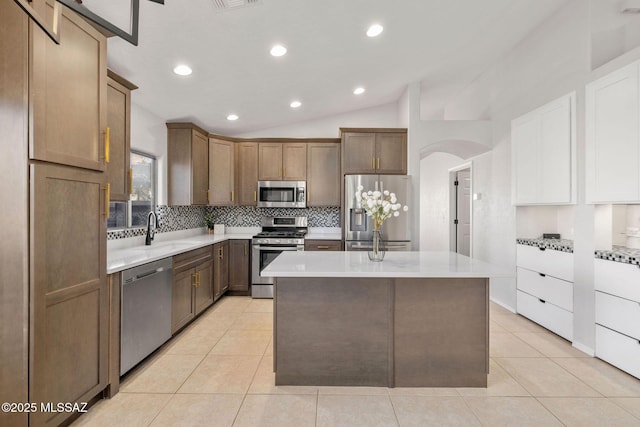 kitchen with light tile patterned flooring, lofted ceiling, sink, a kitchen island with sink, and stainless steel appliances