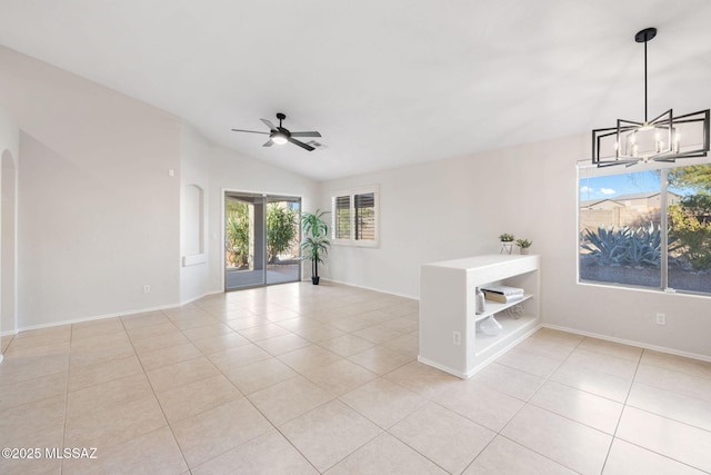 empty room featuring lofted ceiling, ceiling fan with notable chandelier, and light tile patterned floors