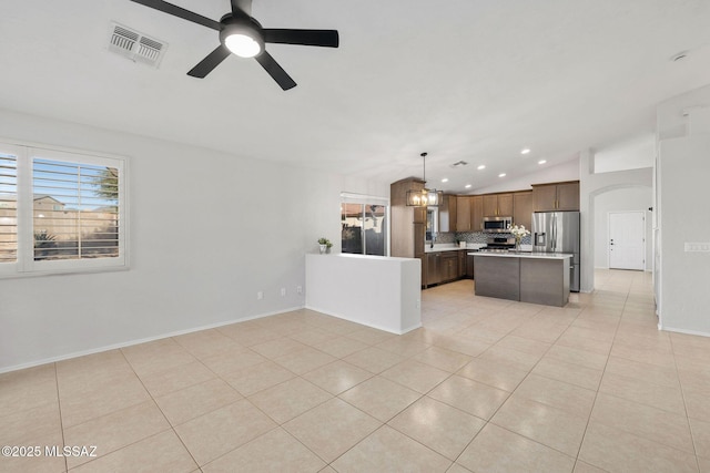 kitchen with light tile patterned floors, hanging light fixtures, stainless steel appliances, a center island, and tasteful backsplash