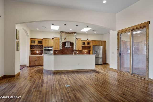 kitchen with appliances with stainless steel finishes, tasteful backsplash, dark hardwood / wood-style flooring, hanging light fixtures, and a kitchen island with sink