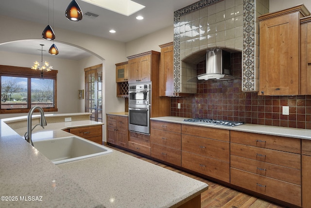 kitchen with sink, stainless steel appliances, tasteful backsplash, decorative light fixtures, and wall chimney exhaust hood