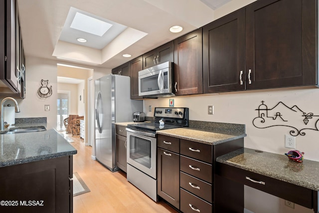 kitchen featuring sink, light hardwood / wood-style flooring, appliances with stainless steel finishes, a raised ceiling, and dark stone counters