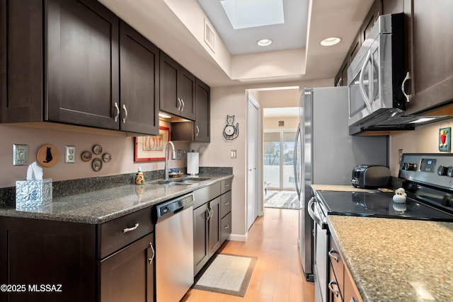 kitchen featuring sink, dark brown cabinets, stainless steel appliances, a skylight, and light wood-type flooring