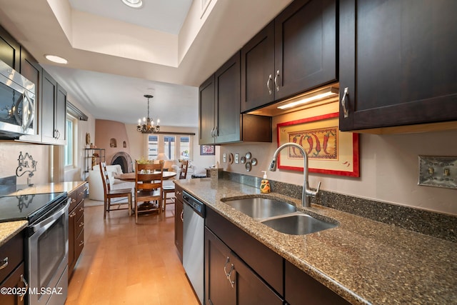 kitchen featuring sink, hanging light fixtures, appliances with stainless steel finishes, dark stone counters, and light hardwood / wood-style floors