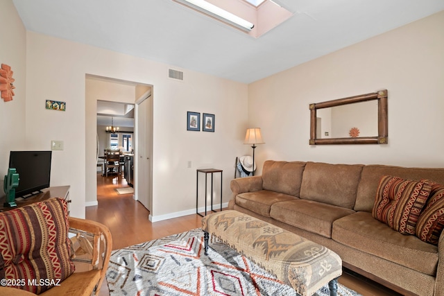 living room with hardwood / wood-style floors, an inviting chandelier, and a skylight