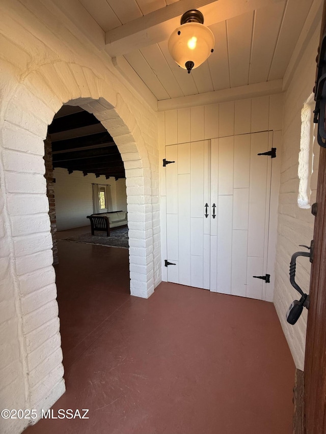 hallway featuring beamed ceiling, brick wall, and wooden ceiling