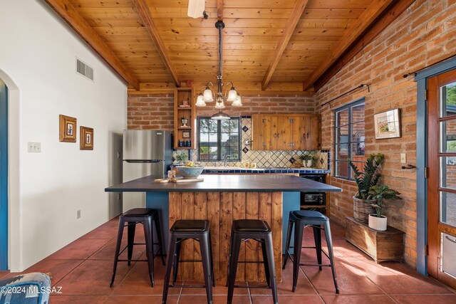 kitchen with wood ceiling, a kitchen breakfast bar, dark tile patterned flooring, brick wall, and beam ceiling