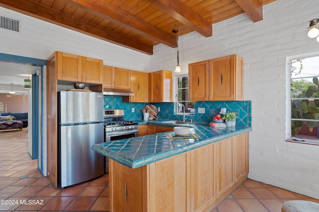 kitchen with appliances with stainless steel finishes, pendant lighting, sink, tile counters, and kitchen peninsula