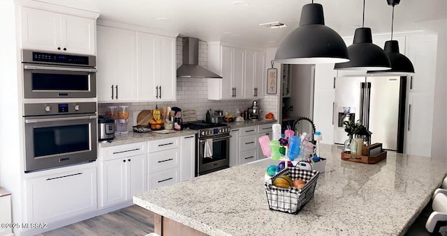 kitchen with stainless steel appliances, light stone countertops, white cabinets, and wall chimney exhaust hood