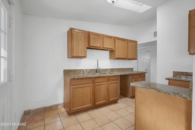 kitchen featuring light stone counters, sink, light tile patterned floors, and lofted ceiling with skylight