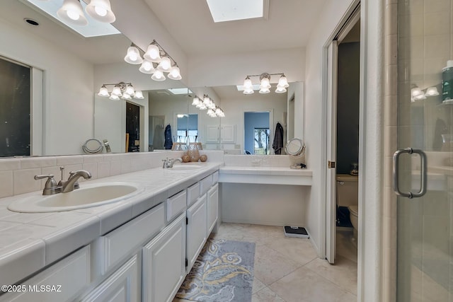 bathroom with toilet, a skylight, vanity, a shower with door, and tile patterned flooring
