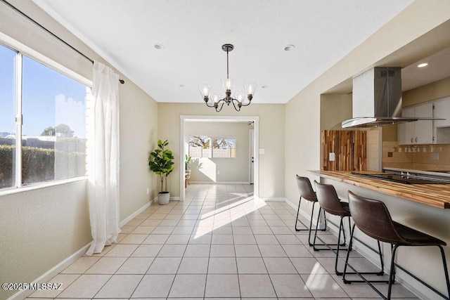 kitchen with light tile patterned floors, a breakfast bar area, island range hood, black electric cooktop, and decorative backsplash