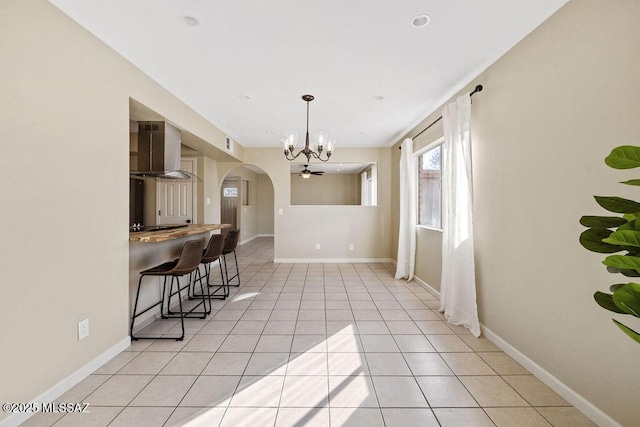 kitchen featuring wooden counters, a chandelier, a kitchen bar, light tile patterned floors, and wall chimney range hood