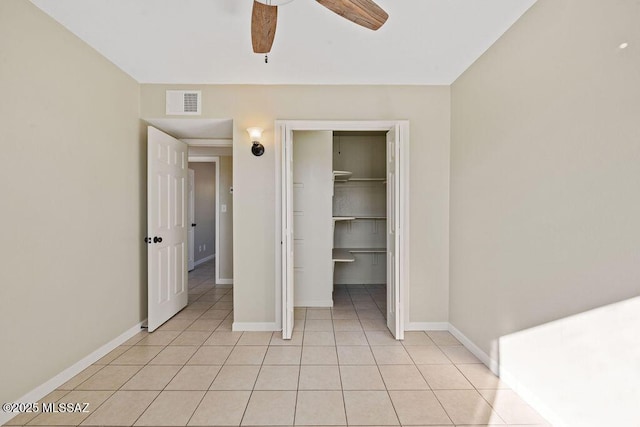 unfurnished bedroom featuring light tile patterned flooring, a walk in closet, ceiling fan, and a closet