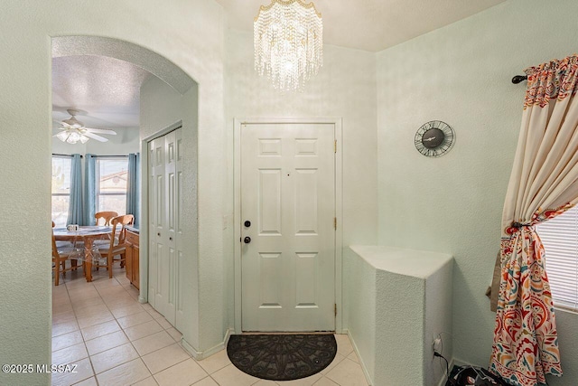 foyer with ceiling fan with notable chandelier, a textured ceiling, and light tile patterned flooring