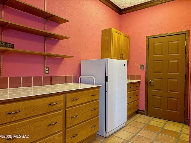 kitchen with tile countertops, ornamental molding, and white fridge