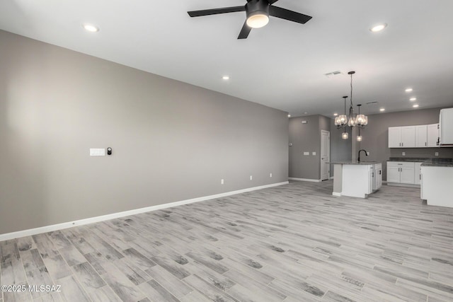 unfurnished living room featuring sink, ceiling fan with notable chandelier, and light hardwood / wood-style floors