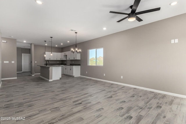 kitchen featuring decorative light fixtures, light hardwood / wood-style floors, an island with sink, ceiling fan with notable chandelier, and white cabinets