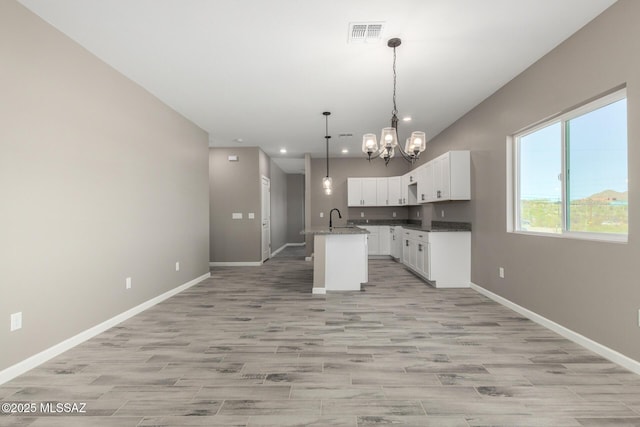 kitchen featuring decorative light fixtures, white cabinetry, a chandelier, a center island with sink, and light wood-type flooring