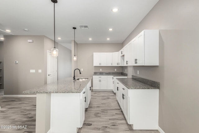 kitchen with sink, white cabinetry, a kitchen island with sink, dark stone countertops, and decorative light fixtures