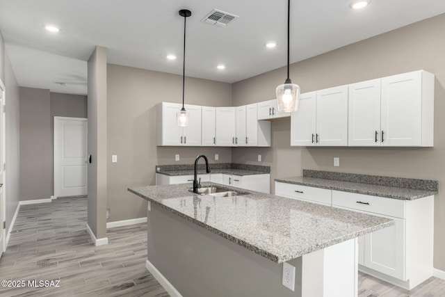 kitchen with pendant lighting, sink, an island with sink, and white cabinets