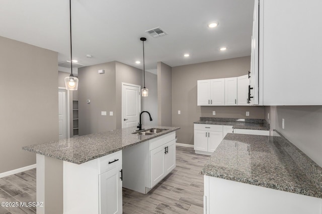 kitchen with hanging light fixtures, white cabinetry, a kitchen island with sink, and sink