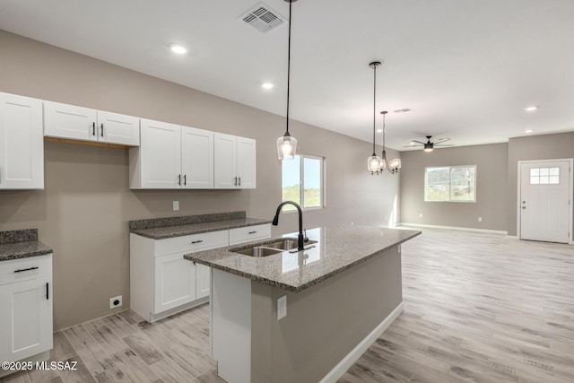 kitchen featuring white cabinetry, decorative light fixtures, sink, and a center island with sink