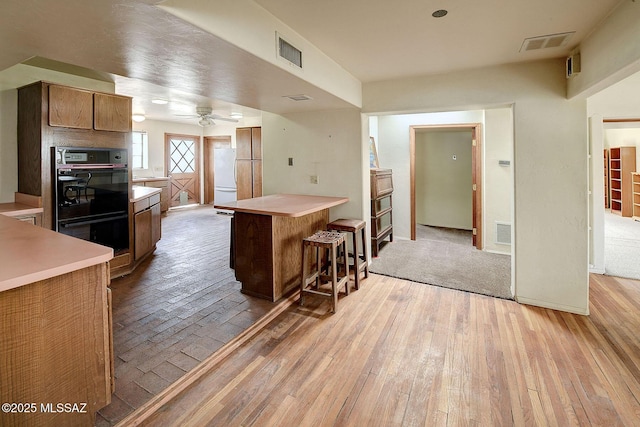 kitchen with a breakfast bar area, light hardwood / wood-style flooring, white refrigerator, a kitchen island, and black double oven