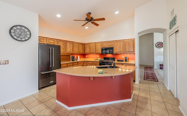 kitchen featuring sink, a breakfast bar area, an island with sink, ceiling fan, and black appliances