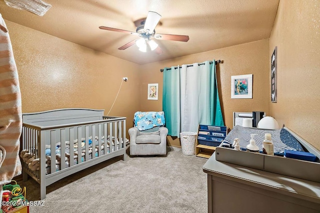 carpeted bedroom with a nursery area, a textured ceiling, and ceiling fan