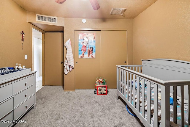 carpeted bedroom featuring a nursery area, ceiling fan, and a closet