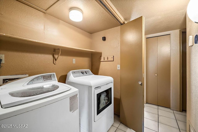 clothes washing area featuring light tile patterned flooring, washing machine and dryer, and a textured ceiling