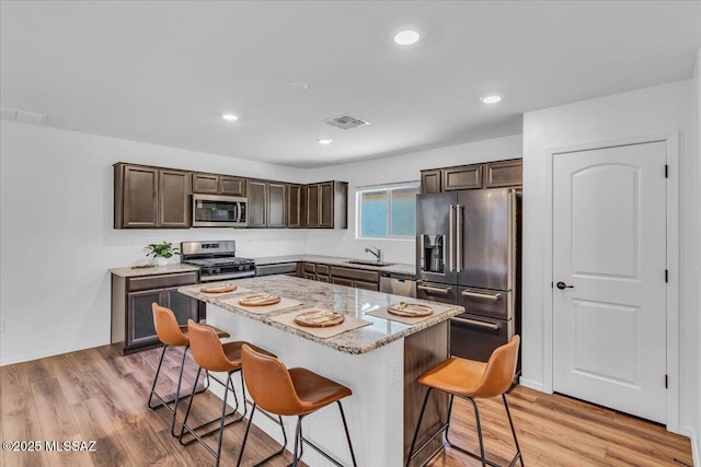 kitchen featuring visible vents, dark brown cabinetry, light wood-style floors, a breakfast bar area, and appliances with stainless steel finishes