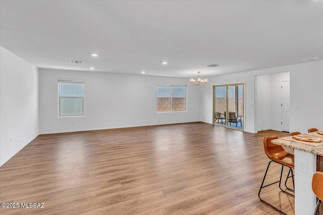 unfurnished living room featuring light wood-style floors, plenty of natural light, recessed lighting, and a chandelier