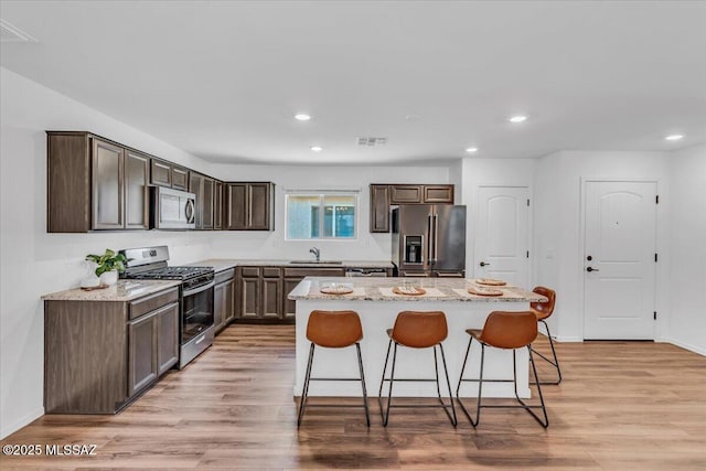 kitchen with dark brown cabinetry, appliances with stainless steel finishes, a breakfast bar, a center island, and recessed lighting