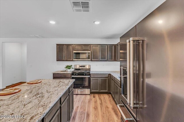 kitchen with stainless steel appliances, visible vents, dark brown cabinets, light wood-type flooring, and a kitchen bar