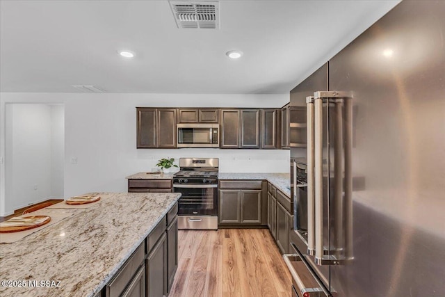 kitchen with dark brown cabinets, light stone counters, stainless steel appliances, light wood-type flooring, and visible vents