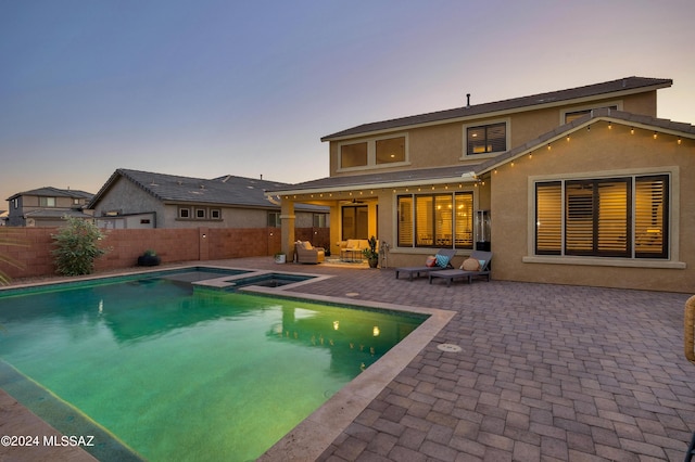 back house at dusk with a swimming pool with hot tub, an outdoor living space, and a patio