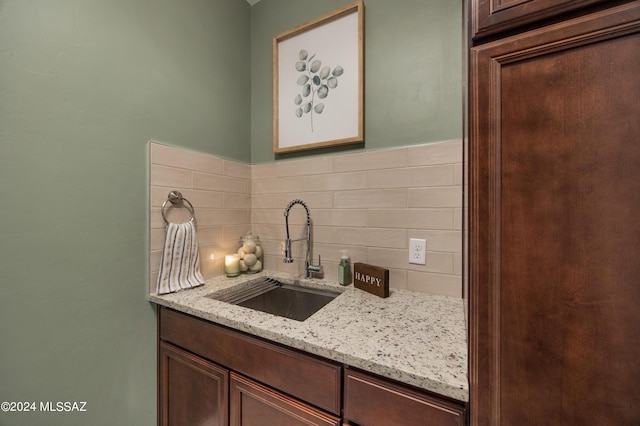 kitchen featuring dark brown cabinetry, light stone countertops, sink, and backsplash