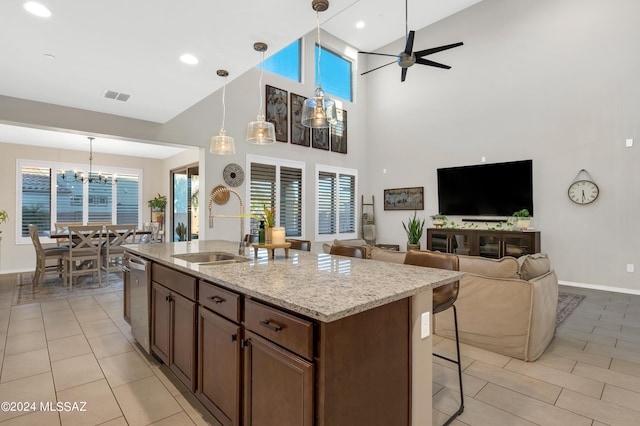 kitchen with pendant lighting, sink, light stone countertops, an island with sink, and stainless steel dishwasher