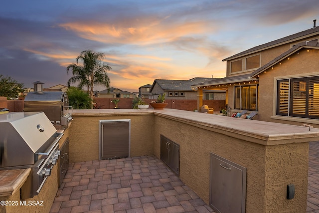 patio terrace at dusk with area for grilling and an outdoor kitchen