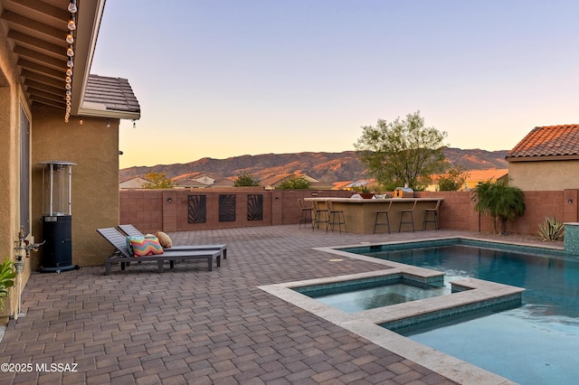 pool at dusk featuring an in ground hot tub, exterior bar, a mountain view, and a patio