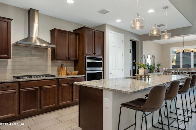 kitchen featuring light stone counters, a kitchen island with sink, and wall chimney range hood