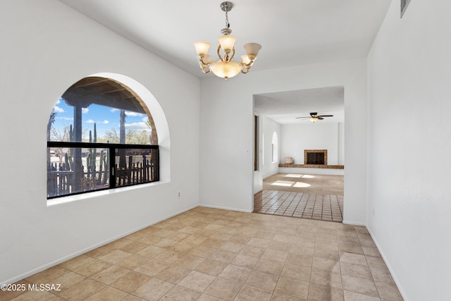 unfurnished room with a brick fireplace and ceiling fan with notable chandelier