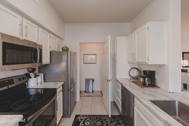 kitchen with light tile patterned flooring, white cabinetry, backsplash, light stone counters, and stainless steel appliances