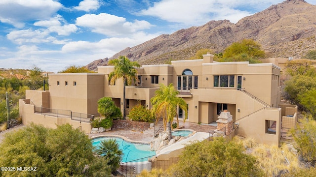 rear view of property featuring a swimming pool with hot tub, a mountain view, a patio, and a balcony